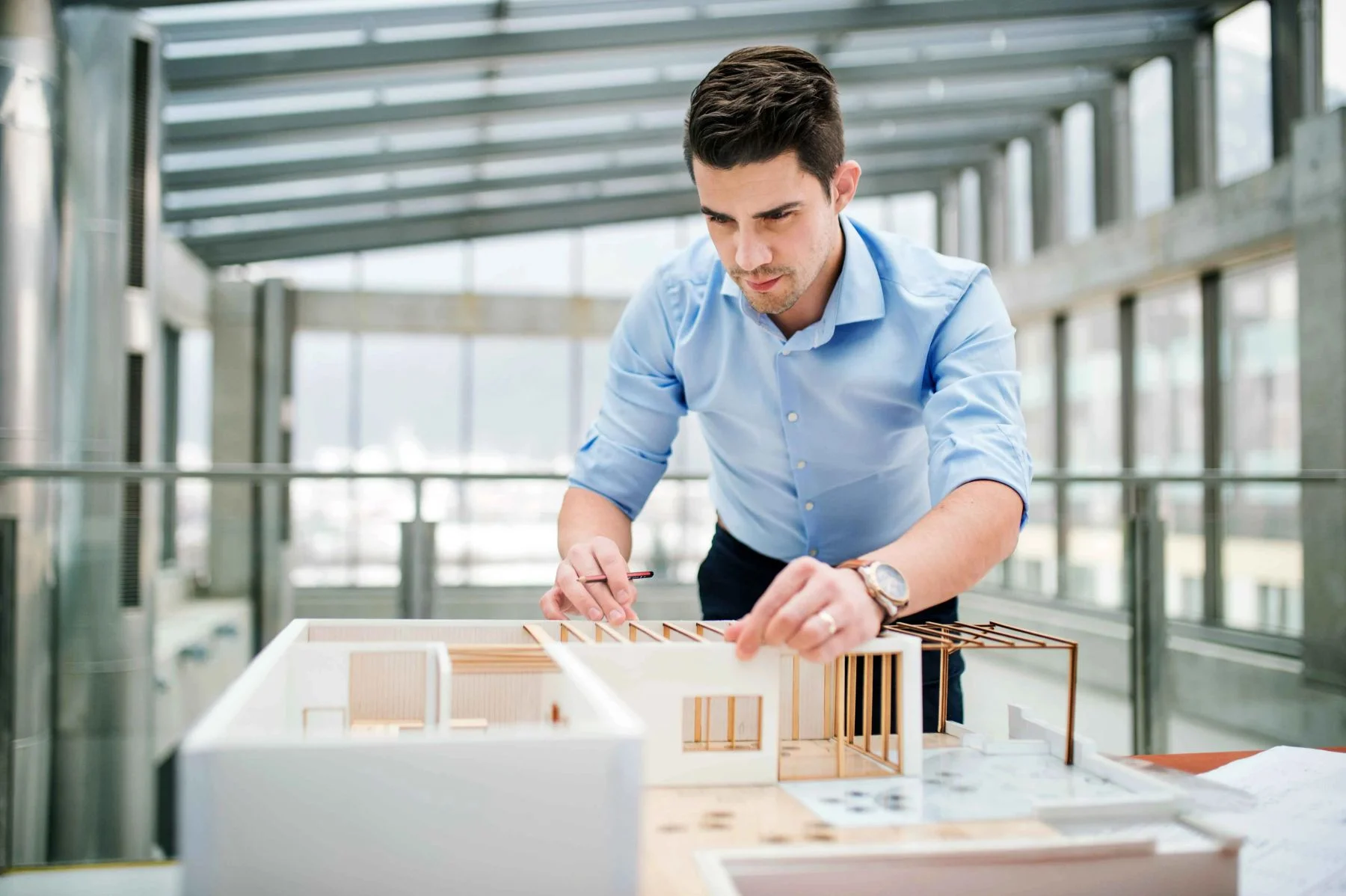 Junger Geschäftsmann oder Architekt mit Modell eines Hauses, das im Büro steht und arbeitet.